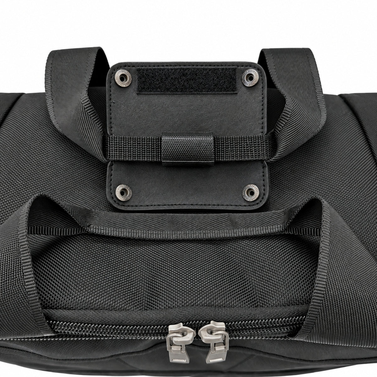 Close-up of a black duffel bag showing a front zippered compartment with dual silver zipper pulls and a black webbing handle attachment with metal rivets on a white background.